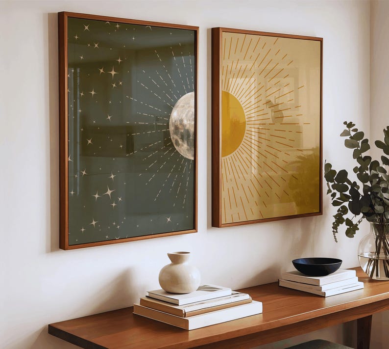 Two framed celestial prints hanging above a wooden console table styled with stacked books, a ceramic vase, and a vase of eucalyptus leaves.