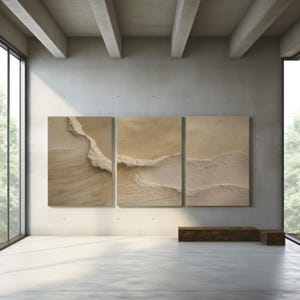 Może przedstawiać: Trzyczęściowa abstrakcyjna sztuka ścienna z teksturowanymi beżowymi i kremowymi wzorami przypominającymi fale. Grafika jest prezentowana w nowoczesnym, minimalistycznym wnętrzu z dużymi oknami i betonową podłogą. Ogólna estetyka jest neutralna i uspokajająca.