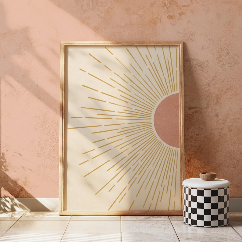 A framed abstract sun print in wooden frame leaning against a textured peach wall above a tiled floor.