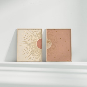 Two framed sun and moon posters placed side-by-side on a white surface against a plain wall.