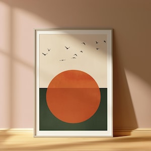 May include: A framed art print with a minimalist landscape design. The artwork shows a cream-coloured sky, a large orange sun, and a dark green lower section. Silhouetted birds are depicted flying across the sky, adding a natural element.