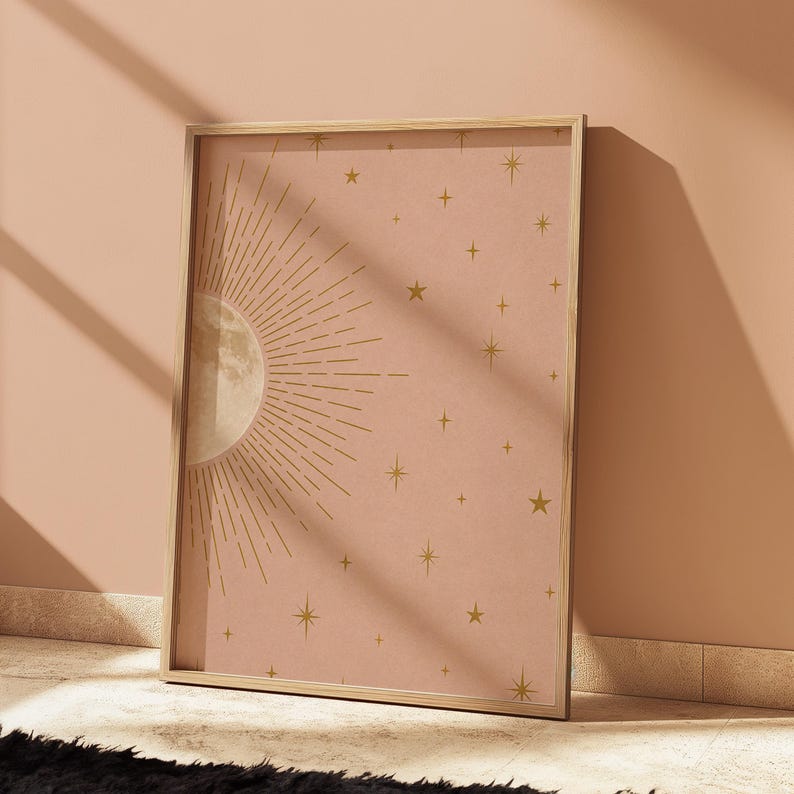 A framed moon and stars print in a wooden frame leaning on a tiled floor against a peach wall.