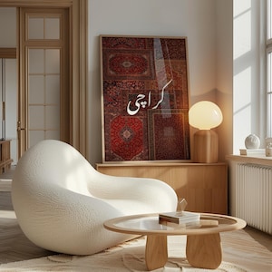 May include: A framed artwork featuring a collage of red and brown carpet patterns with the word "Karachi" in white script. The artwork is displayed above a wooden cabinet, next to a mushroom-shaped lamp. A white, textured armchair and a round coffee table complete the scene.