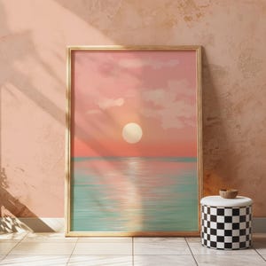 May include: A framed art print of a sunset over the sea. The sky is a gradient of pink and orange with a large white sun. The sea is a light teal colour, and the print is in a gold frame. A black and white chequered stool is in the foreground.