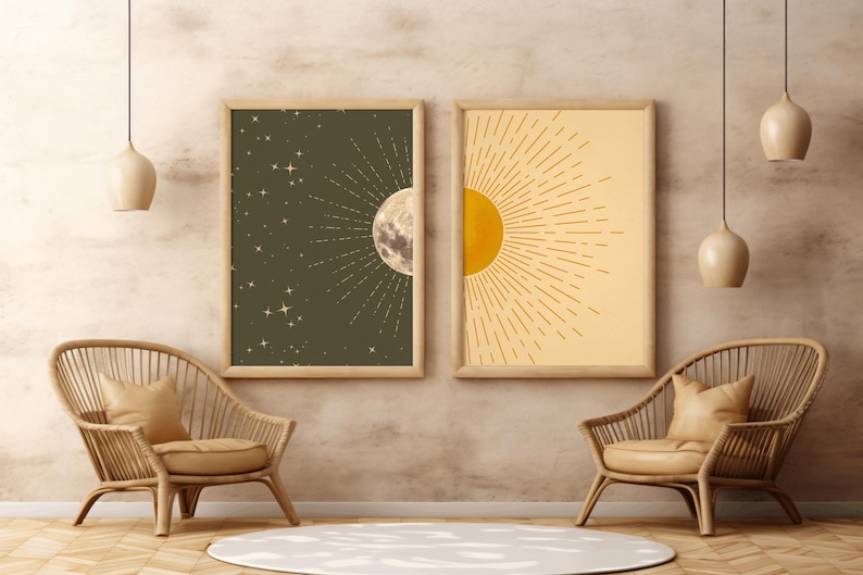 Two framed celestial art prints featuring a dark green moon and star background on the left and a yellow sunburst on the right, hanging on a textured wall between two rattan chairs.