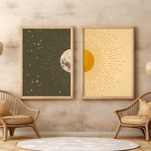 Two framed celestial art prints featuring a dark green moon and star background on the left and a yellow sunburst on the right, hanging on a textured wall between two rattan chairs.