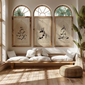 May include: Three framed wall art pieces with Arabic calligraphy in black script. The art is displayed above a wooden bench with white pillows. The room has arched windows and a large potted plant, creating a bright and airy atmosphere.