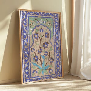 Puede incluir: Obra de arte enmarcada con un diseño floral detallado. La obra tiene un fondo beige con un motivo floral central en azul y marrón. El borde es azul vibrante con detalles blancos, todo dentro de un marco dorado.
