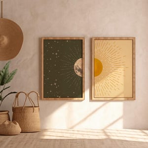 Two framed sun and moon posters mounted on a textured plaster wall in a room with woven baskets, a potted plant, and a straw hat hanging on the left.