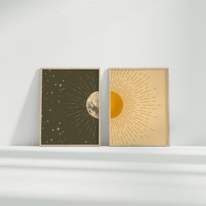 Two framed prints of a moon and sun displayed side by side on a plain white surface under soft lighting.