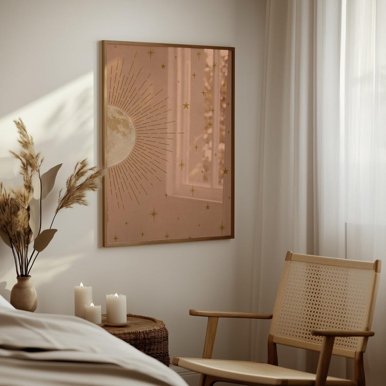 A single framed moon and star print hangs on a wall next to a window, with a woven chair, dried grasses, and lit candles in the foreground.