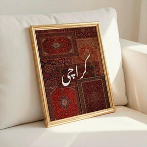 Könnte beinhalten: Ein gerahmter Druck mit einem goldfarbenen Rahmen, der eine Collage von gemusterten Teppichen in Rot-, Braun- und Beigetönen zeigt. Das Wort "Karachi" ist in weißer Schrift geschrieben. Der gerahmte Druck lehnt an einem weißen Sofa.