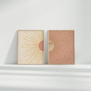 Two framed celestial art prints displayed on a low shelf against a white wall.