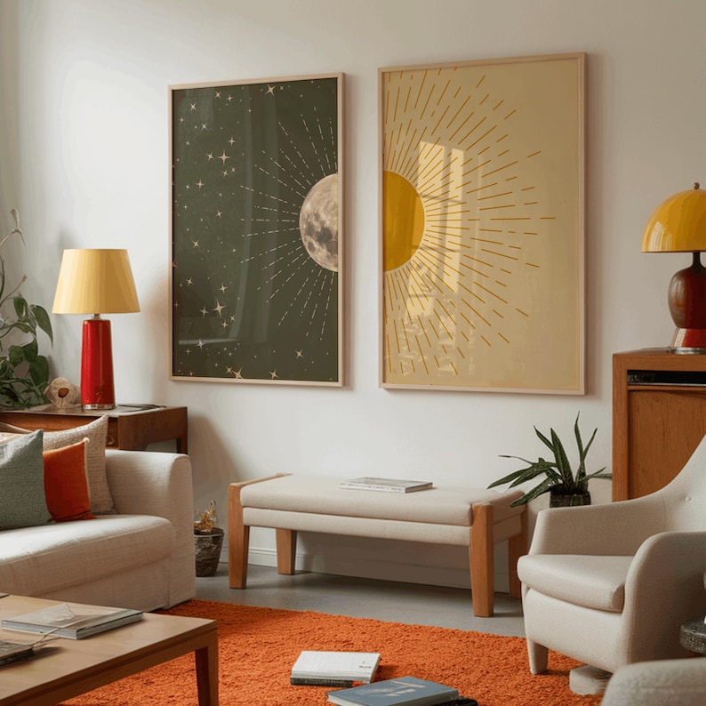 Two framed celestial art prints, one dark green with stars and a half moon and the other yellow with a sunburst, mounted on a white wall above a living room set up with a couch and orange rug.