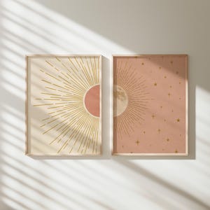 Two framed celestial art prints hang side by side on a light wall with diagonal window light casting shadows across the scene.