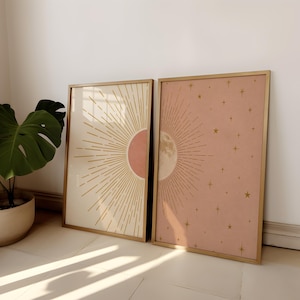 Two framed celestial art prints featuring a sun and moon leaning against a white wall next to a potted plant.