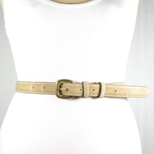 May include: A beige suede belt with a gold-toned buckle. The belt is shown on a white background.