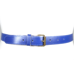 Puede incluir: Un cinturón azul vibrante con una hebilla dorada se muestra en un maniquí blanco. El cinturón está hecho de un material liso y tiene varios agujeros para ajustar. La hebilla es rectangular y tiene un diseño clásico.