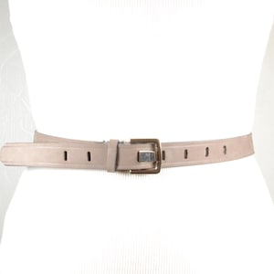 May include: A light brown leather belt with a silver buckle. The belt has a simple design with small holes for adjusting the size.