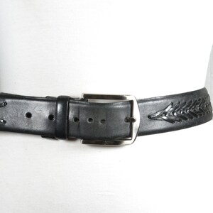 May include: A black leather belt with a silver buckle and a braided design. The belt is woven with a pattern of small, raised lines.