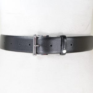 May include: A black leather belt with a silver buckle. The belt is on a white background.