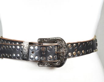 May include: Black leather belt with silver-tone metal studs and a decorative buckle. The belt features a detailed floral design on the buckle and end piece, adding a touch of vintage flair. A stylish accessory.