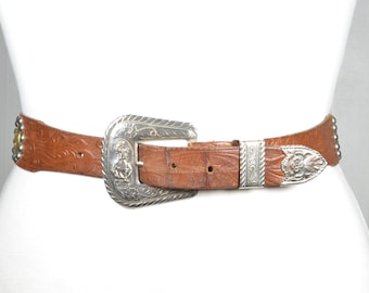 Cinturón vintage de cuero marrón repujado con hebilla western ornamentada y detalles florales con tachuelas, estilo vaquera