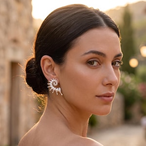 Peut inclure: Une boucle d'oreille argentée présentant un design en spirale rappelant un coquillage, composée de multiples segments incurvés et pointus s'étendant vers l'extérieur depuis un point central, fixée au lobe de l'oreille.