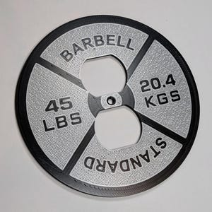 May include: A black and silver standard barbell weight plate with the text "BARBELL" and "STANDARD" printed on it. The weight is 45 lbs or 20.4 kgs.