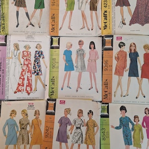 Könnte beinhalten: Eine Sammlung von Vintage-McCall's-Schnittmusterumschlägen. Die Umschläge zeigen Illustrationen von Kleidern, Overalls und Blusen in verschiedenen Stilen. Die Muster sind für Damen, Junioren und Teenager. Die Farben sind lebendig, mit orangefarbenen, grünen, blauen und rosa Kleidern.