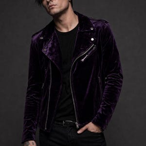 May include: A deep purple velvet jacket with a classic biker style. The jacket features a notched collar, asymmetrical zipper closure, and silver hardware. The model is wearing a black t-shirt and black jeans.