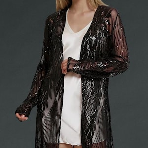 May include: A long, open-front black sequin duster coat. The sheer fabric is adorned with intricate patterns and sparkling sequins. The coat is floor-length and has long sleeves, creating an elegant and eye-catching look. This garment is perfect for layering.