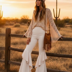 May include: A beige lace long-sleeve top with flared sleeves, white high-waisted trousers featuring ruffled leg details, a brown suede fringe crossbody bag, and a patterned headband worn around the head, creating a coordinated ensemble.