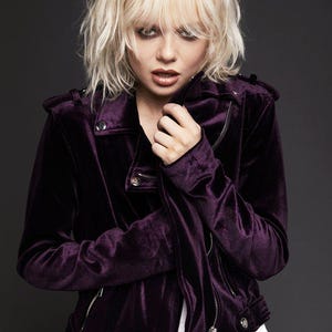 May include: A deep purple velvet jacket with a classic biker style. The jacket features a notched collar, a zipper closure, and silver hardware. The model is wearing a white shirt underneath.