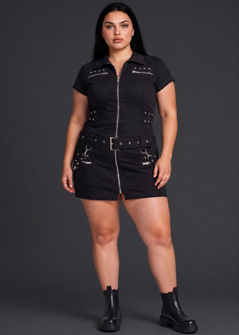 May include: A black short-sleeved mini dress featuring a full-length silver front zipper, a collared neckline, and a matching belt. The garment includes multiple silver-toned metal zippers, eyelets, and buckle details across the chest and skirt.