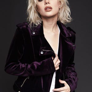 May include: A dark purple velvet jacket with a zipper closure and silver hardware. The jacket has a classic biker style with a notched collar and shoulder epaulets. The model is wearing a white top underneath.
