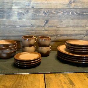 May include: A set of brown and white ceramic mugs and bowls. The mugs have a brown and white swirl design. The bowls are stacked and have a similar design. The set is on a black tablecloth.