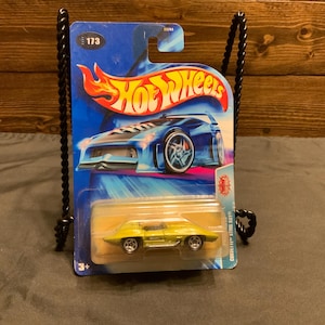 May include: A yellow Hot Wheels Corvette Sting Ray die-cast toy car on a blue and white card with the Hot Wheels logo. The car has black wheels and a black interior. The card has the number 173 on it.