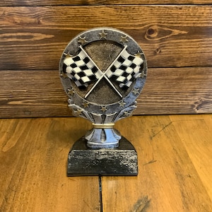 May include: A silver and gold trophy with a checkered flag design. The trophy has a round base with a star pattern and a black base.