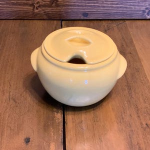 May include: A yellow ceramic serving dish with a lid. The lid has a small hole in the center.