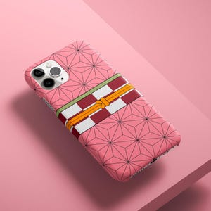 Può includere: Custodia per telefono rosa con motivo geometrico e fascia decorativa a righe rosse, bianche e gialle. La custodia ha un ritaglio per la fotocamera.