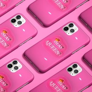 以下が含まれることがあります： ピンクのiPhoneケースに、透明なステッカーが貼られています。ステッカーには「SLAY QUEEN!」と王冠が書かれており、少し盛り上がっていて光沢のある仕上げになっています。