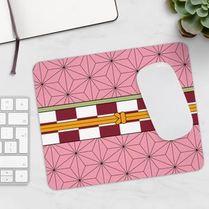 May include: A pink mousepad with a geometric pattern of intersecting lines and a decorative band featuring a checkered design in burgundy and white, with a yellow and green accent. A white computer mouse rests on the pad.
