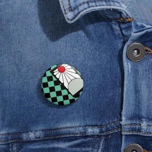 Könnte beinhalten: Ein runder Ansteckbutton mit farbenfrohem Design. Der Button zeigt ein schwarz-türkises Schachbrettmuster, eine weiße Blume mit roter Mitte und eine graue Fächerform. Der Button befindet sich auf einer blauen Jeansjacke.