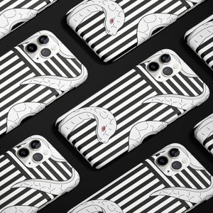 Può includere: Custodie per smartphone con un design a serpente bianco su sfondo a righe bianche e nere. Il serpente ha un occhio rosso. Le custodie sono disposte su una superficie nera.