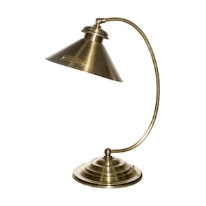 May include: A brass desk lamp with a curved arm and a conical shade. The lamp has a round base. The design is reminiscent of vintage industrial lighting. The lamp's shade has a small label.
