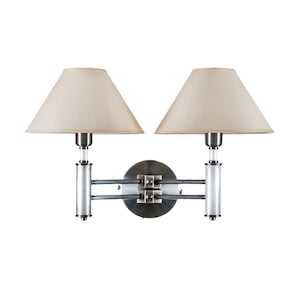 Könnte beinhalten: Doppelte Wandleuchte mit gebürsteter Silberoberfläche. Sie hat zwei beige konische Lampenschirme und eine kreisförmige Montageplatte. Die Leuchte hat ein modernes Design, geeignet für die Innenbeleuchtung.