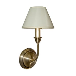 Könnte beinhalten: Eine Wandleuchte mit cremefarbenem Lampenschirm und Messing-Finish. Die Leuchte hat einen gebogenen Arm und einen kreisförmigen Sockel. Der Lampenschirm ist konisch und die Leuchte ist für eine einzelne Glühbirne konzipiert.