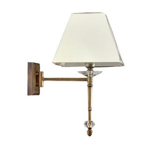 May include: A wall-mounted lamp with a cream-colored lampshade. The lamp features a bronze-colored metal arm and base, with crystal-like accents. The rectangular wall mount has a textured design.