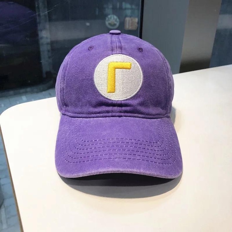 May include: A purple baseball cap with a curved brim. The cap features a white circular patch with a yellow "L" design. The hat is made of a soft material and has a classic six-panel design.